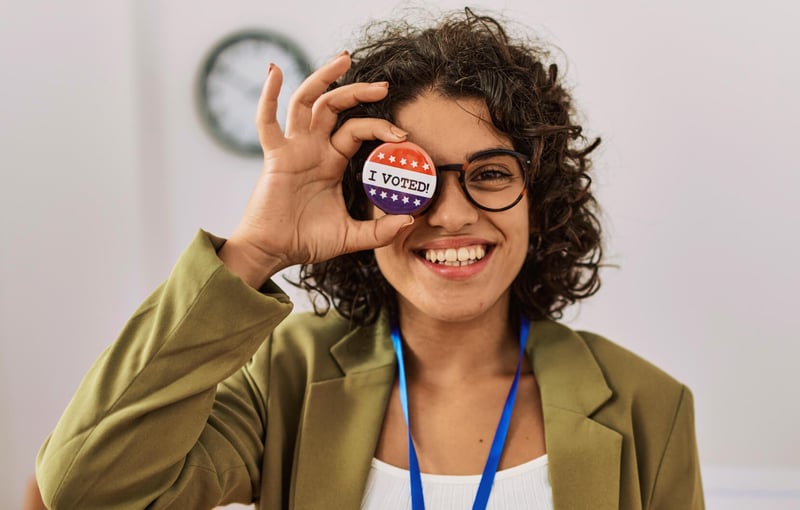 Smiling woman with an 'I voted' badge over her right eye